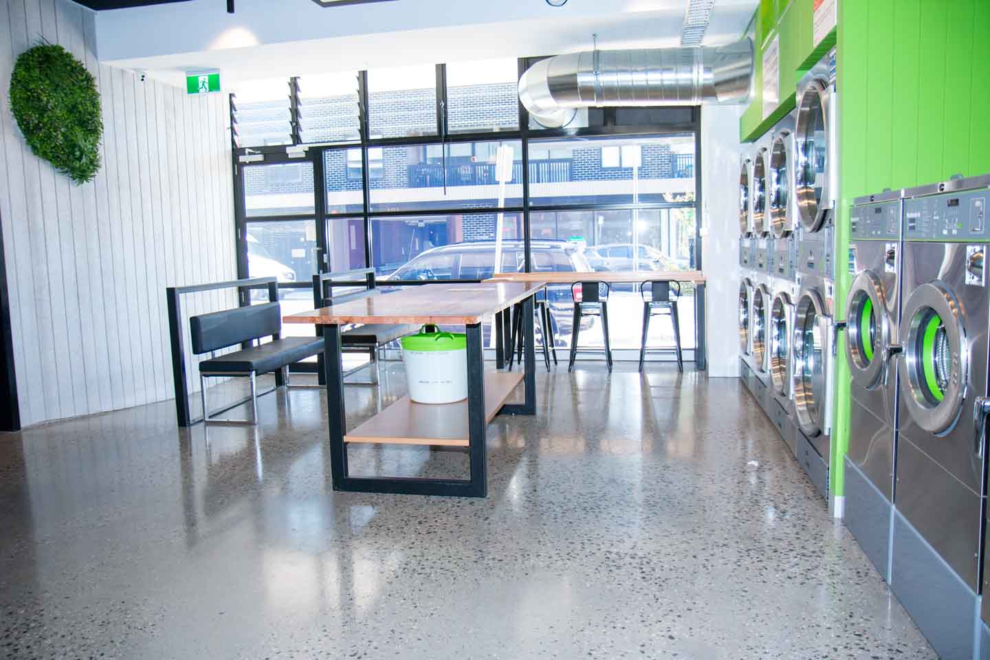 Inside Preston Laundry House — polished concrete floors, a communal folding table by big windows, and rows of modern washers and dryers